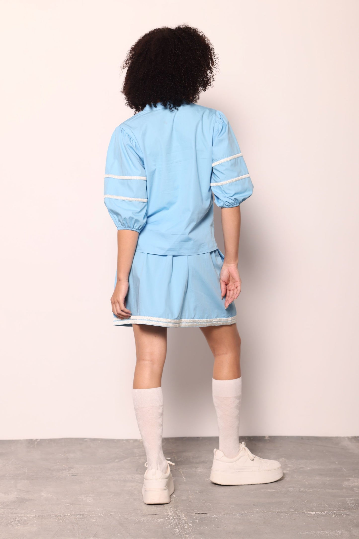 Maude Vivante Noah Top in sky blue with white stripe sleeve detailing, back view, worn with matching pleated skirt and white knee socks.