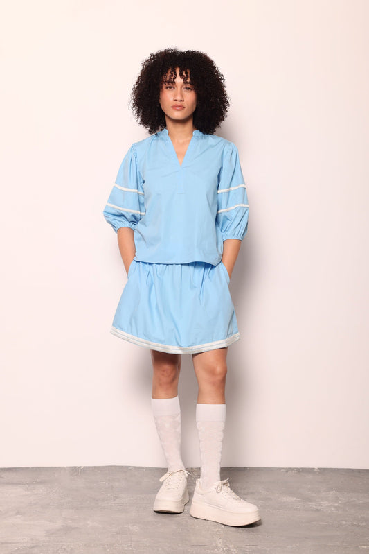 Maude Vivante Noah Top in sky blue with puff sleeves, white trim detailing, V-neckline, worn with matching blue mini skirt and white knee socks.