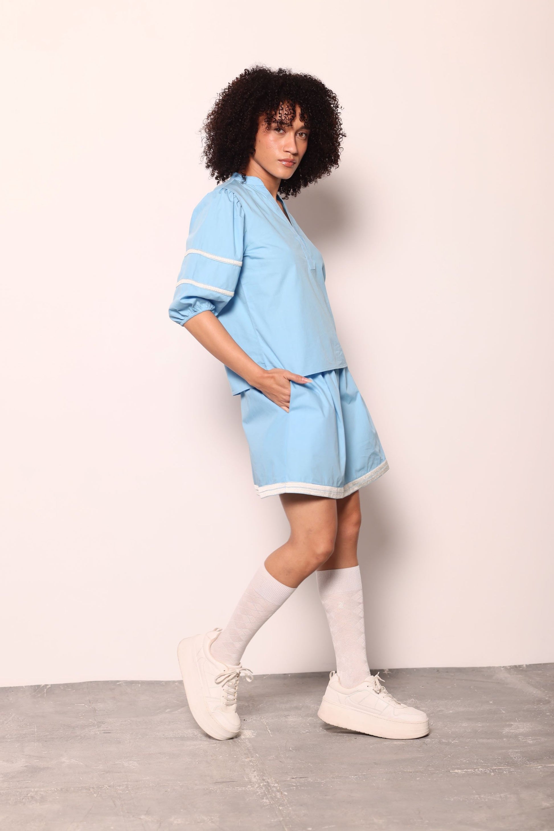 Maude Vivante Noah Top in sky blue with white stripe trim, V-neck, puff sleeves, worn by model with matching shorts and white sneakers.
