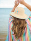 Shiraleah Vitamin Sea Sun Hat shown from back, worn by model at beach, straw hat with colorful embroidery and teal zigzag brim trim.