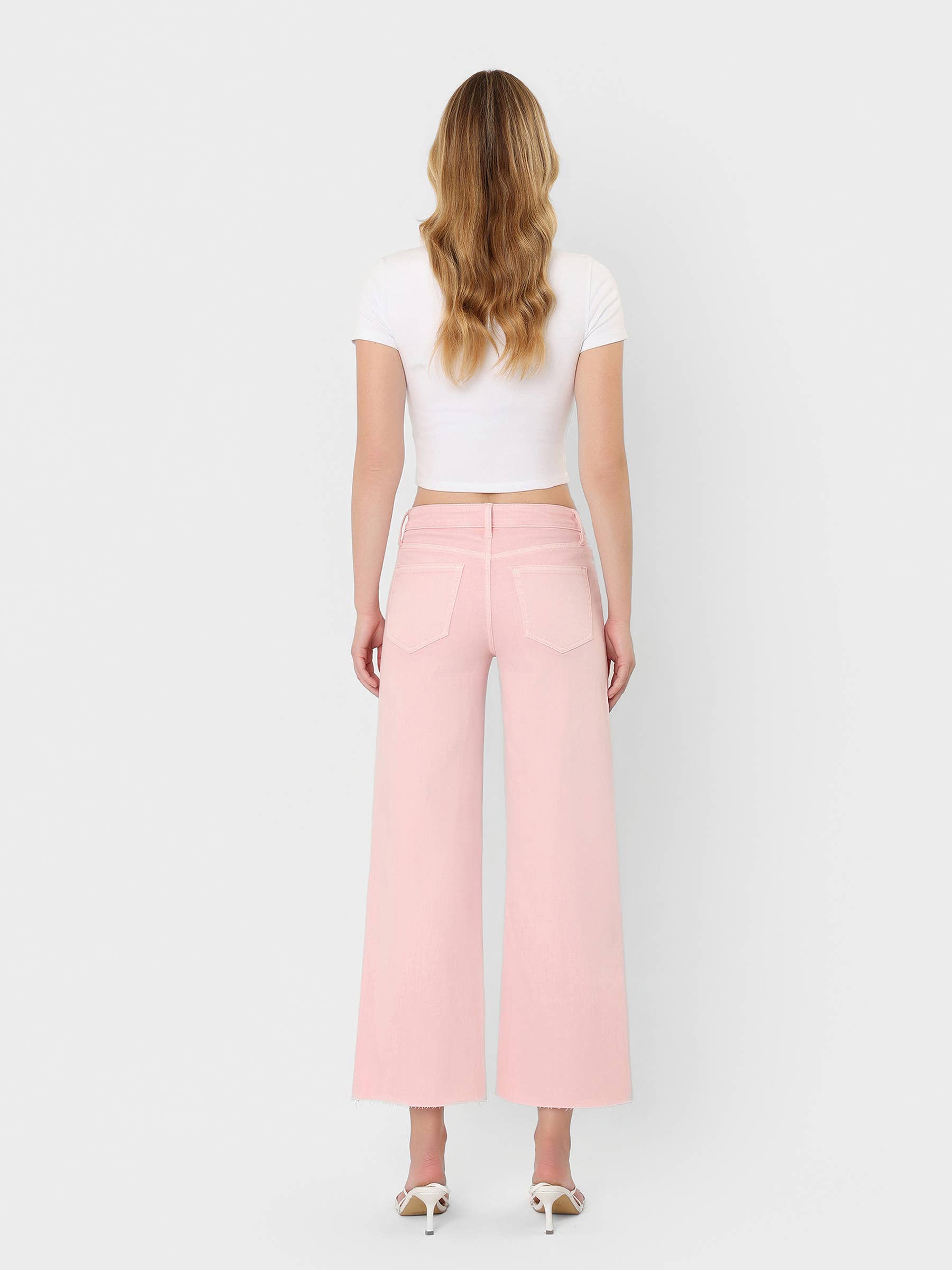 High Rise Crop wide leg bubblegum pink jeans with raw hem, styled with white crop top and heels, back view.