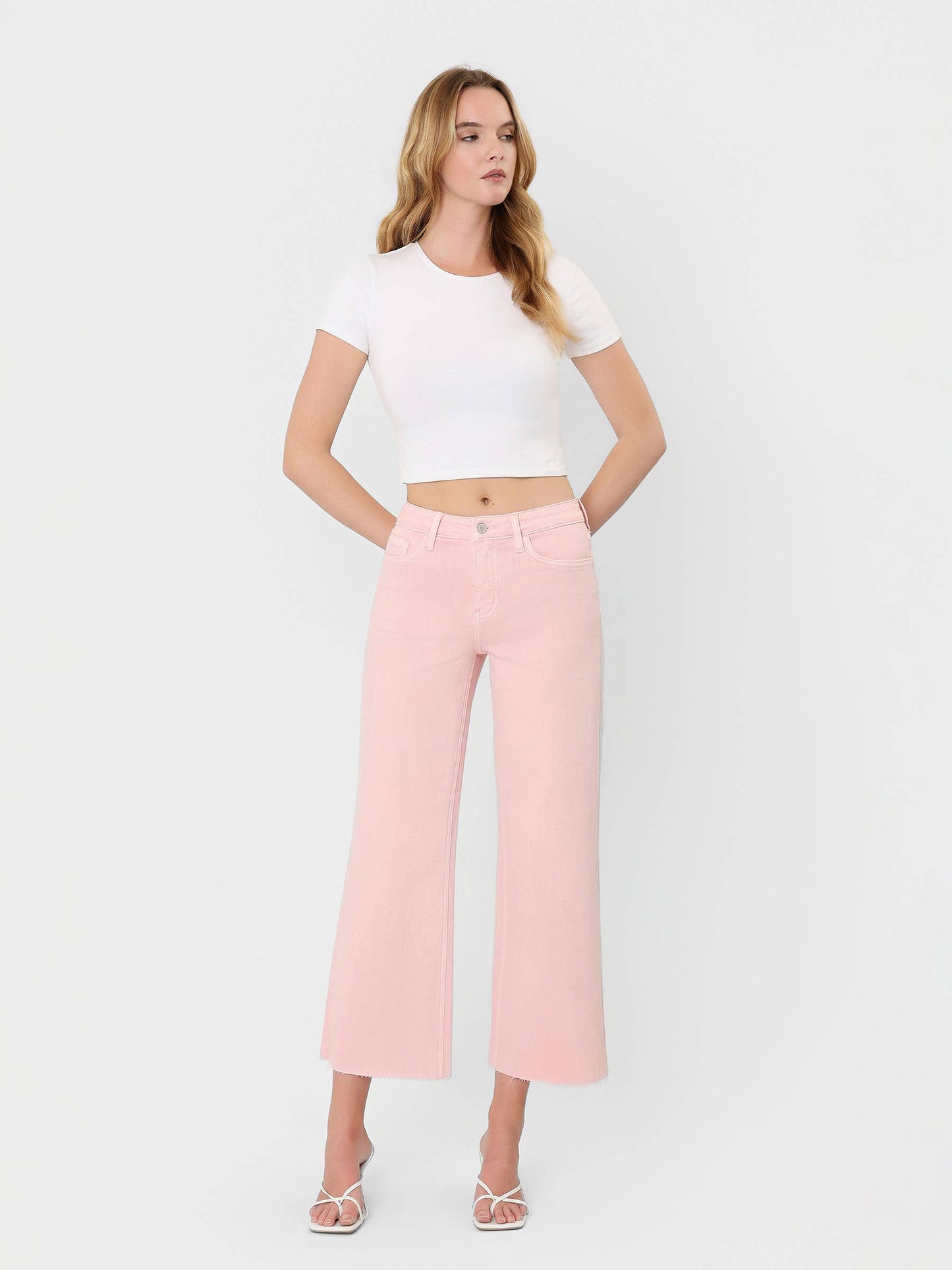 High Rise Crop wide leg cropped jeans in bubblegum pink with raw hem, styled with white crop tee and strappy heels.
