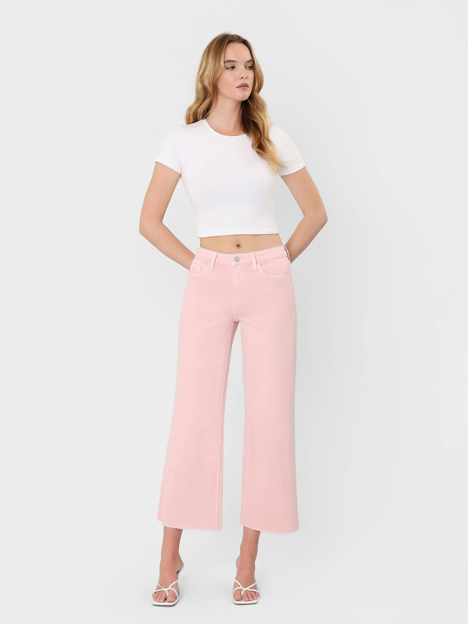 High Rise Crop wide leg cropped jeans in bubblegum pink with raw hem, styled with white crop tee and strappy heels.