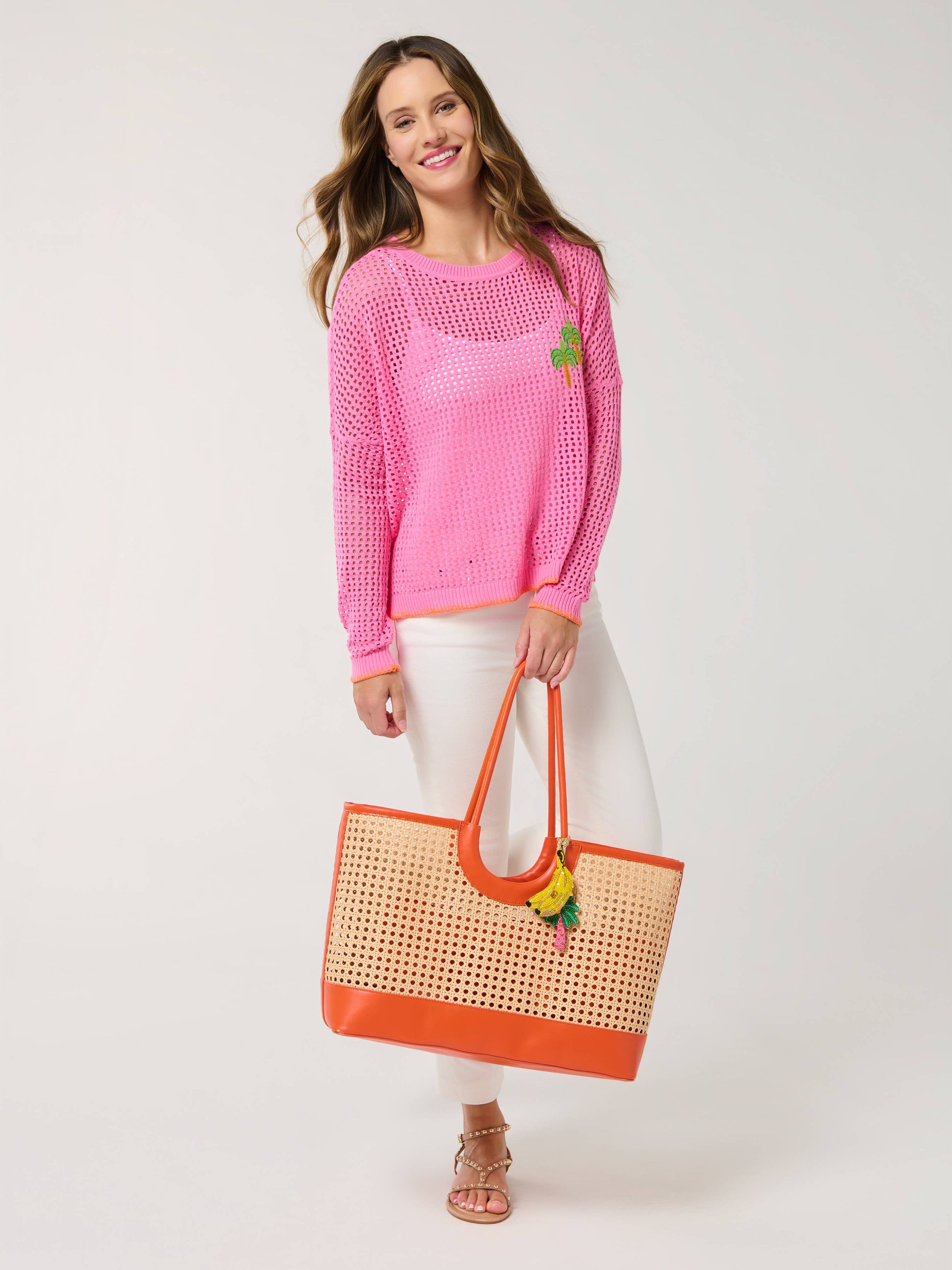 Lyra Tote woven rattan tote bag with orange leather trim, handles, and fruit charm accent.