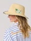 Out Of Office straw fedora sun hat with embroidered palm tree and slogan, worn by smiling blonde woman.
