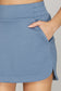 SHE+SKY High Waist Skort with Pockets in steel blue, close-up showing elastic waistband, side pocket, and hem slit.