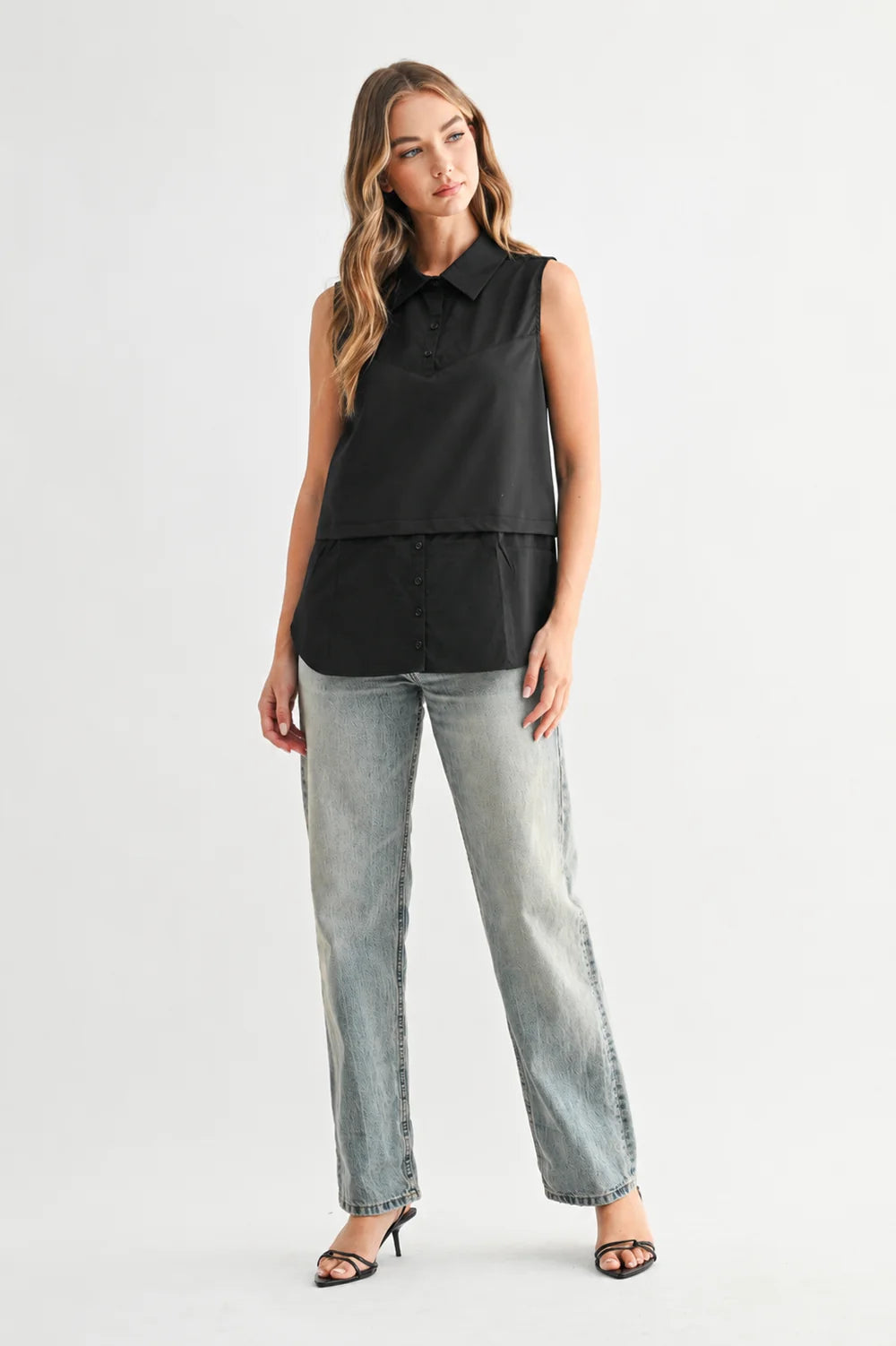 Caroline sleeveless black collared button-up top with layered hem, styled with light wash straight-leg jeans.