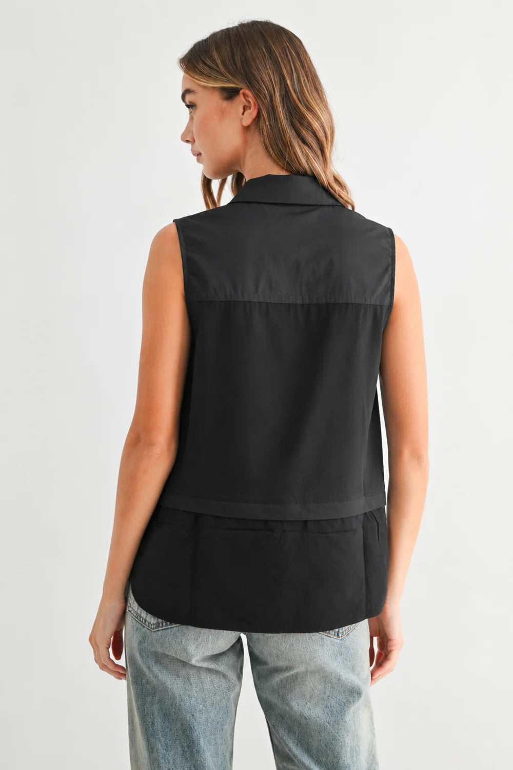 Caroline sleeveless black collared top with layered back detail, paired with light wash jeans.