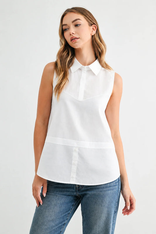 Caroline sleeveless white collared button-front shirt top with layered hem detail, styled with blue jeans.