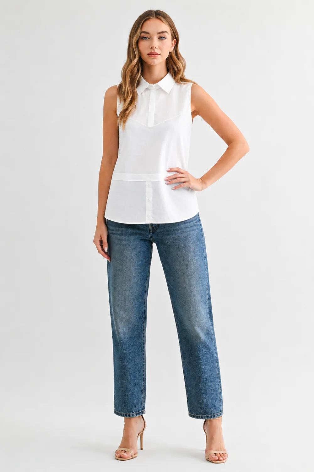 Caroline sleeveless white collared button-front top styled with blue straight-leg jeans and nude heels.
