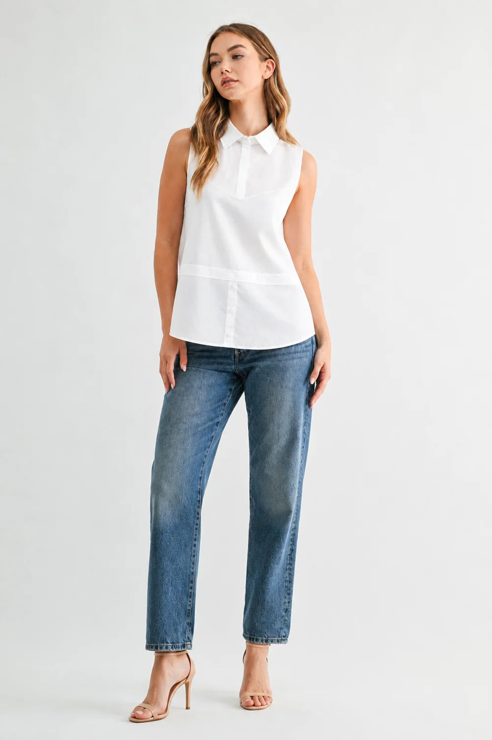 Caroline sleeveless white collared button-front top styled with blue straight-leg jeans and nude heeled sandals.
