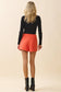 TCEC Side Hidden Zipper Skort in orange, back view on model paired with black ribbed top and ankle boots.