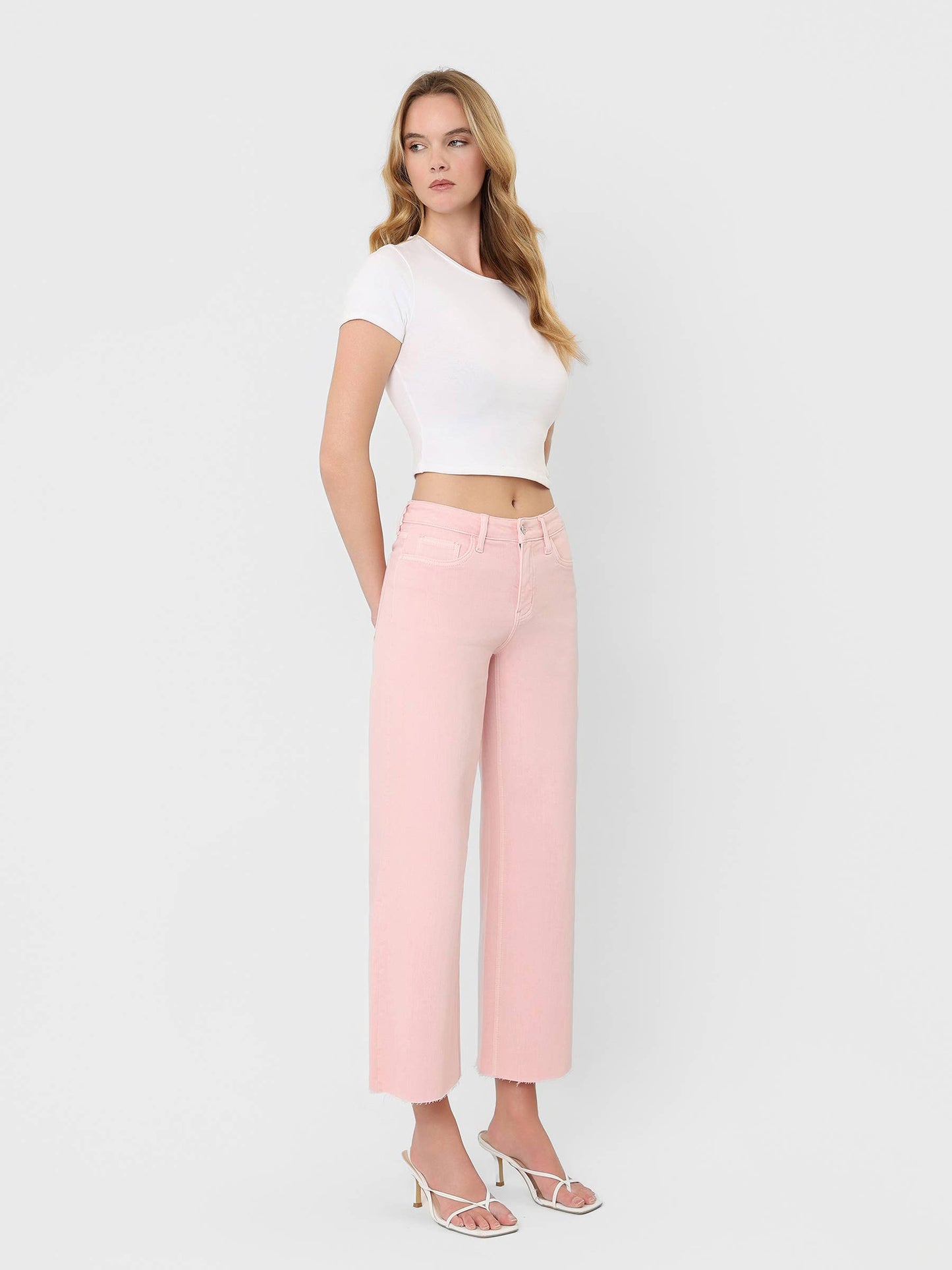 High Rise Crop wide leg jeans in bubblegum pink with raw hem, paired with white crop top and strappy heels.