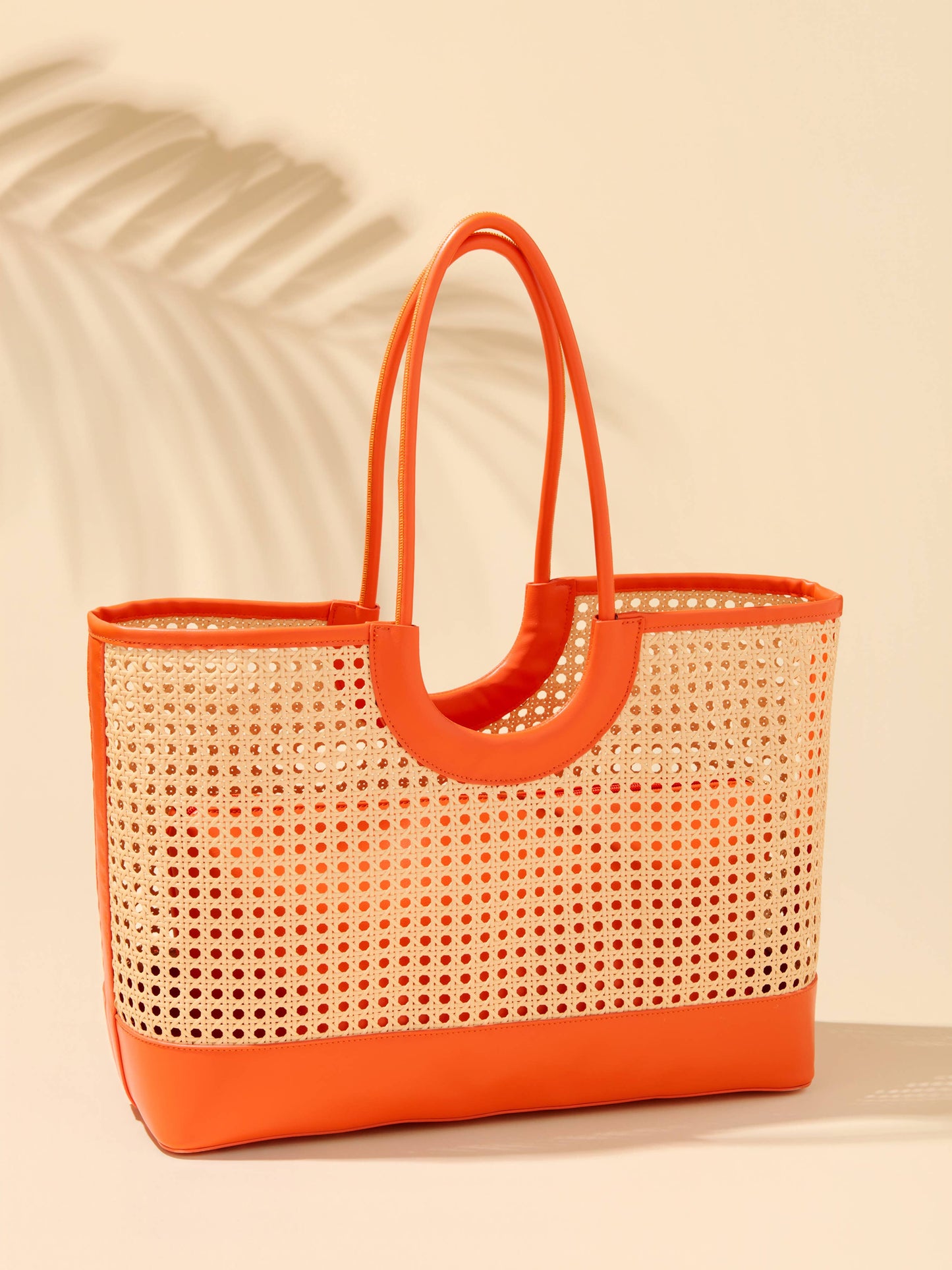 Lyra Tote bag featuring woven rattan body with orange leather trim, handles, and structured base.