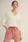 Cloud Kiss Top: women's oversized white V-neck sweater with cropped three-quarter sleeves, paired with red striped shorts.