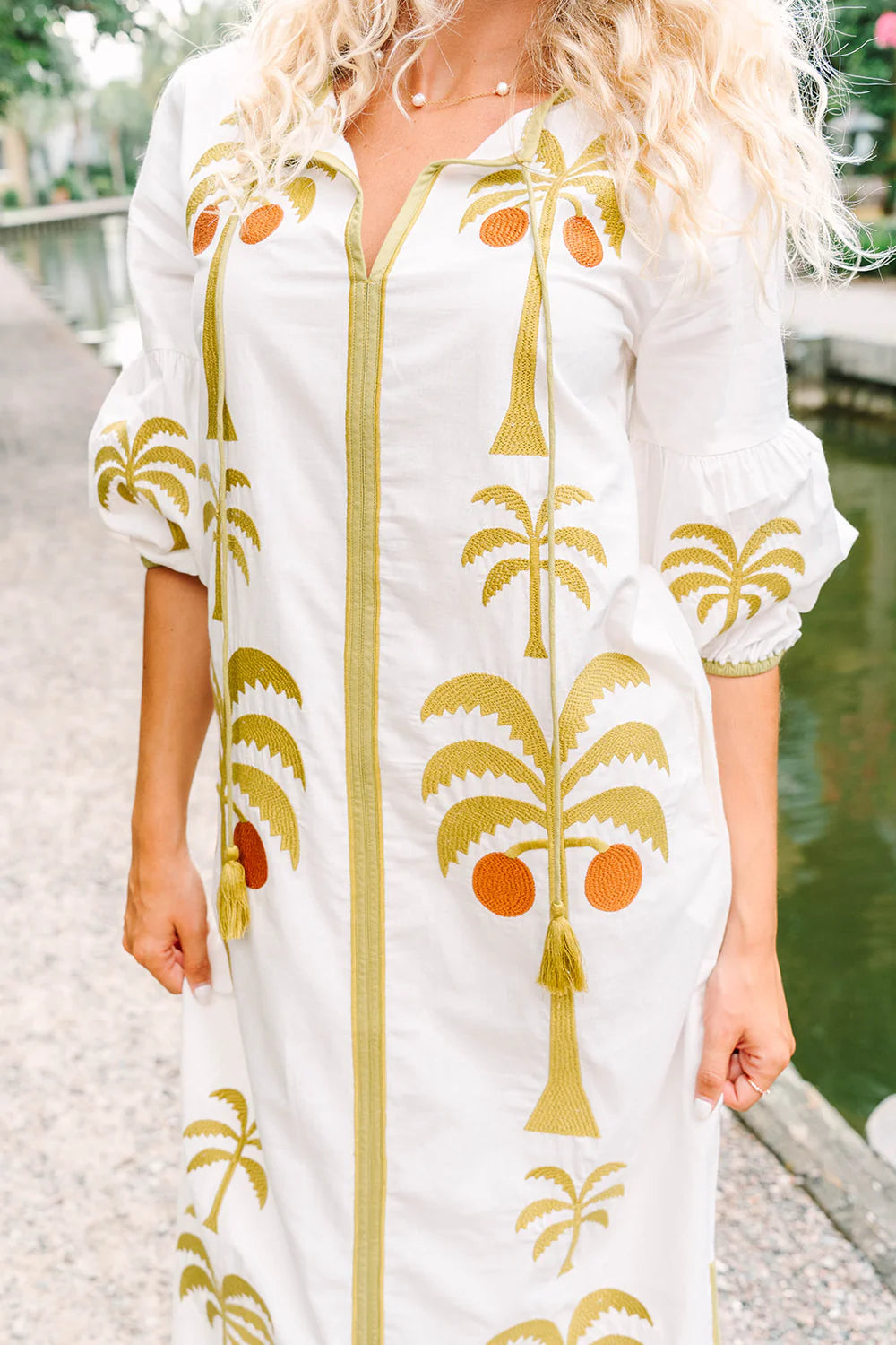 Victoria Dunn Esme white maxi dress with embroidered palm trees, orange fruits, and tassel tie neckline detail.