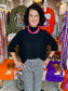 The Maple Mockneck Sweater Black ribbed knit top with pleated flutter sleeves, worn by a smiling woman.