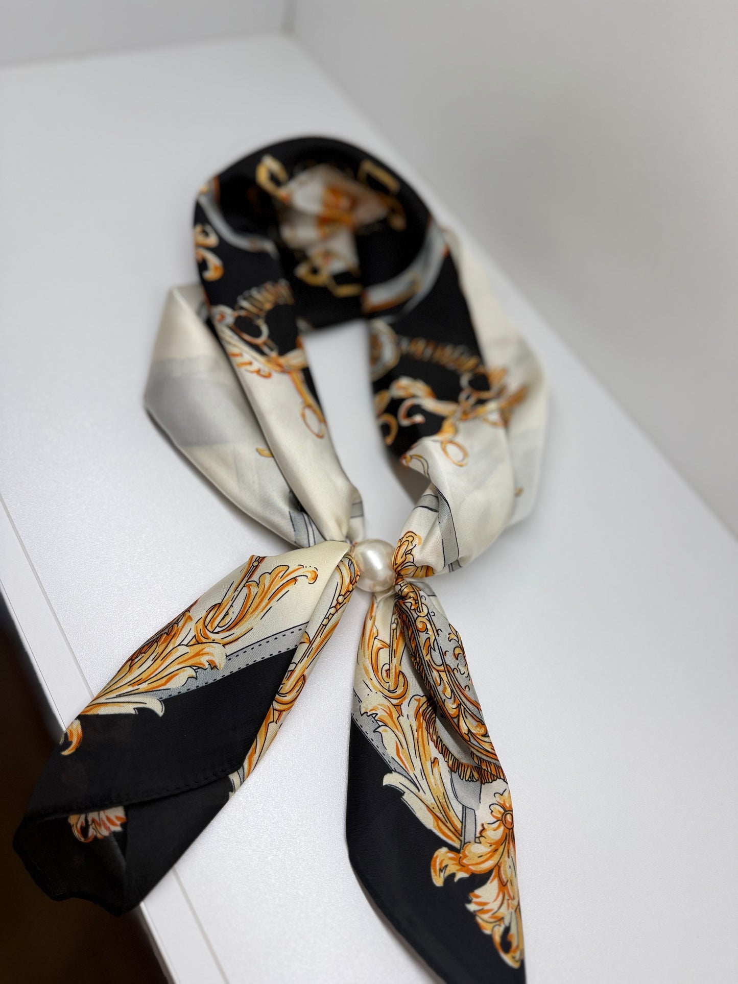Ready To Wear magnetic scarf with baroque gold print, pearl brooch fastening, draped on white surface.
