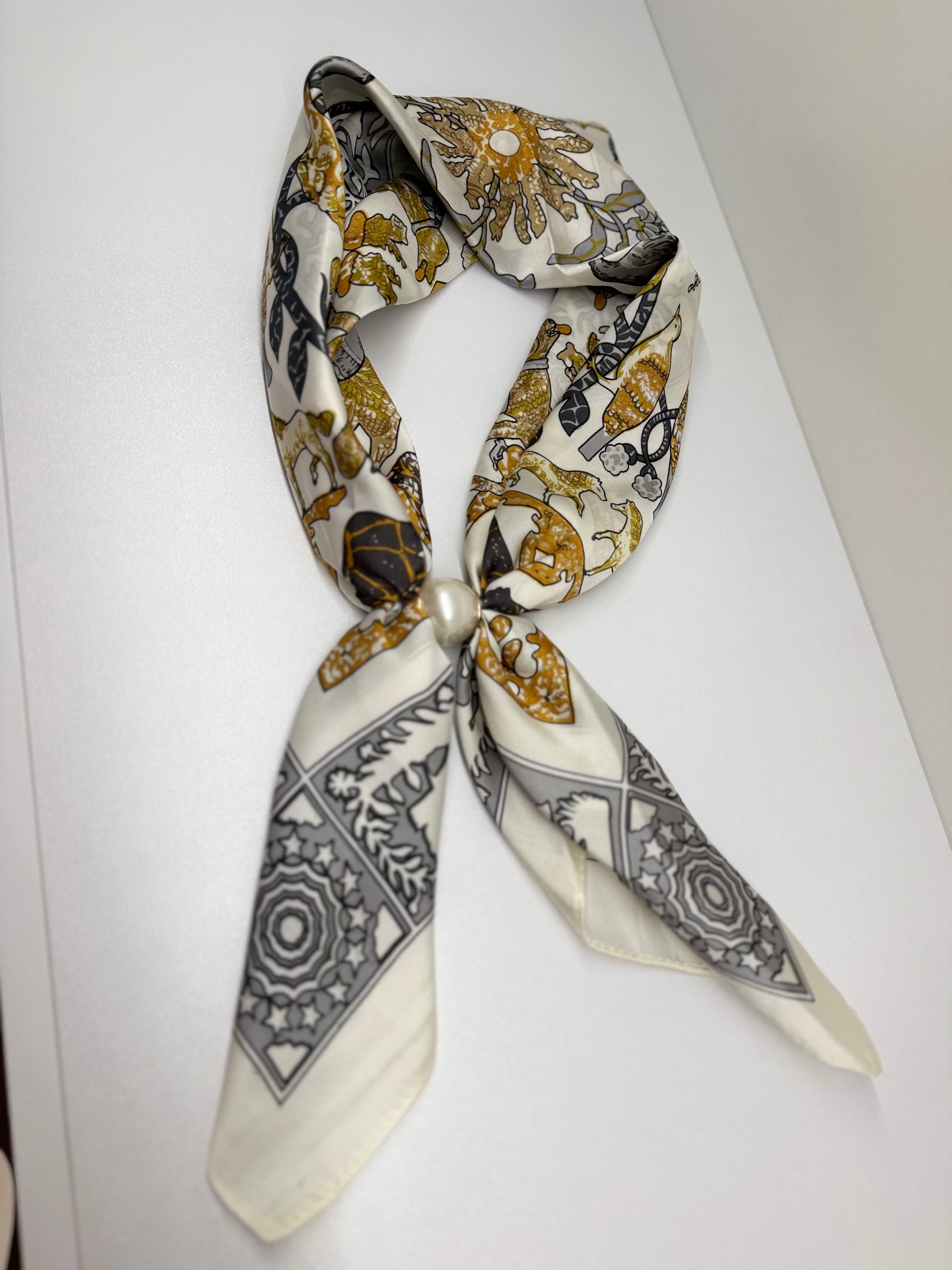 Ready To Wear magnetic silk scarf featuring gold and grey animal print, tied with a pearl closure.