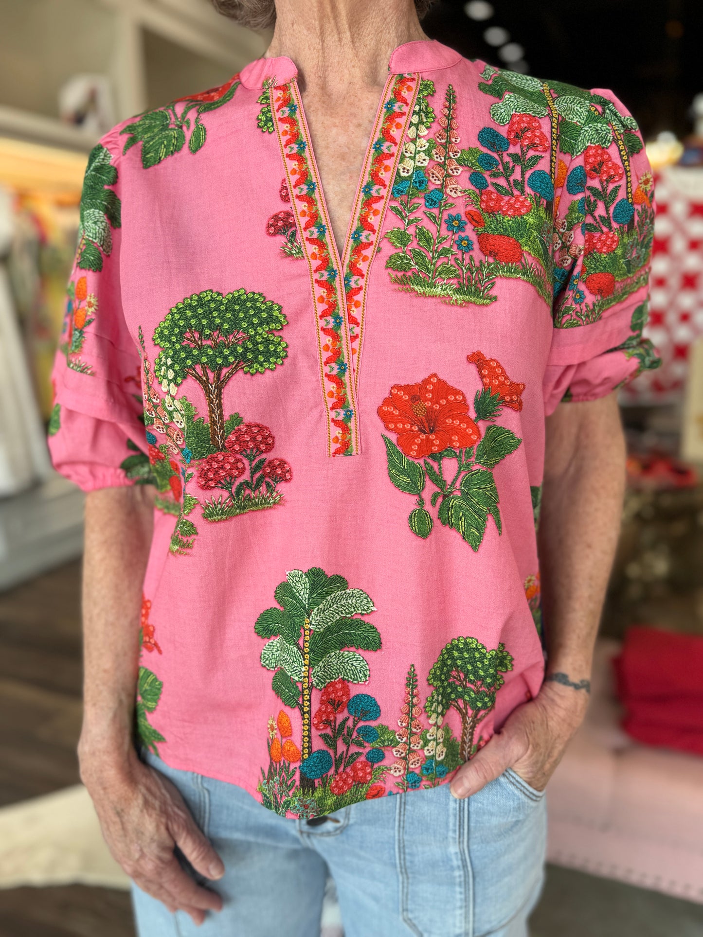 Maude Vivante Raya Top Pink Isles — pink short-sleeve blouse with vibrant botanical embroidery and V-neckline trim.
