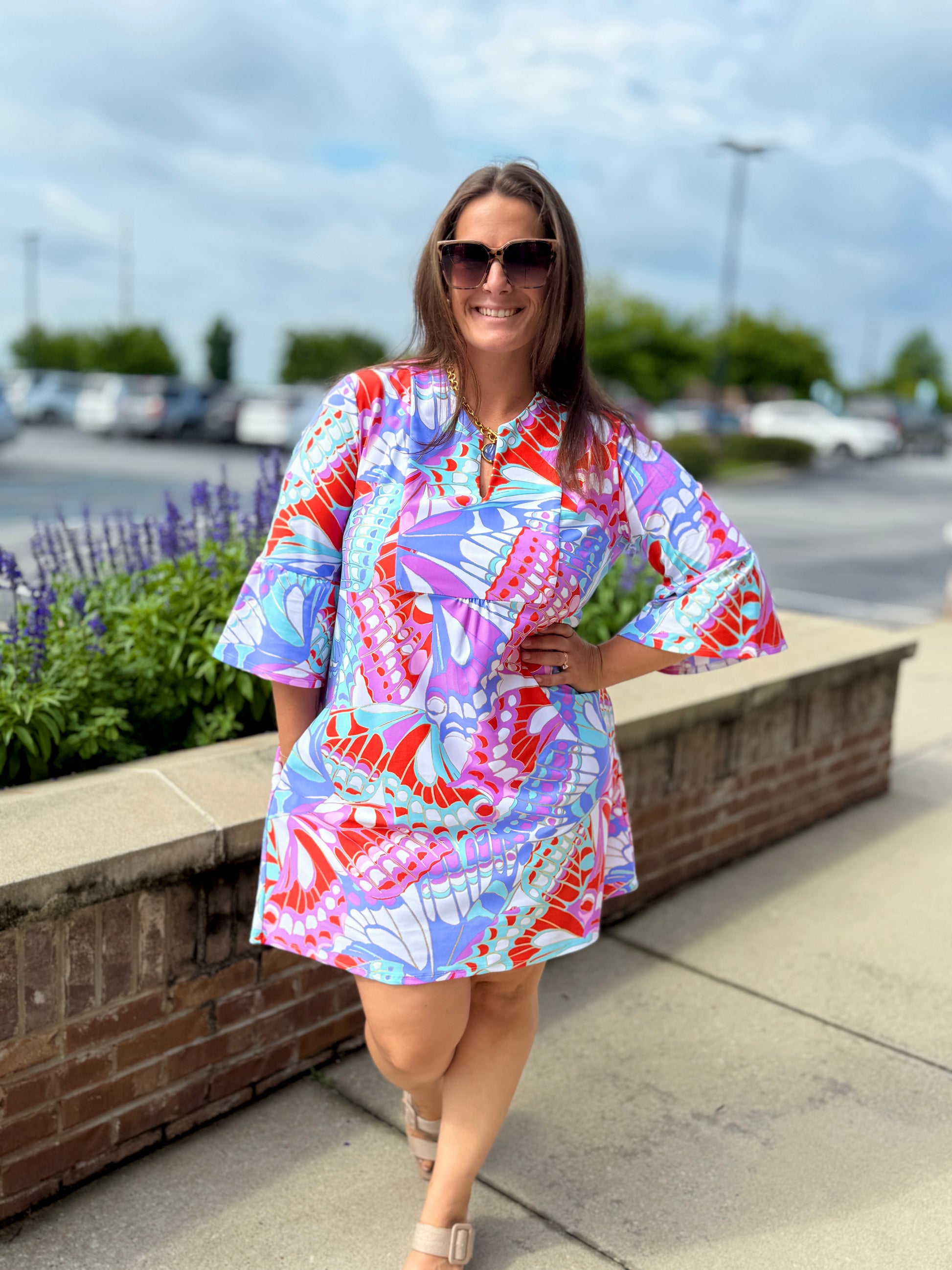 Jude Connally Kerry dress featuring a bold butterfly mosaic print with flutter sleeves, worn by a smiling woman outdoors.