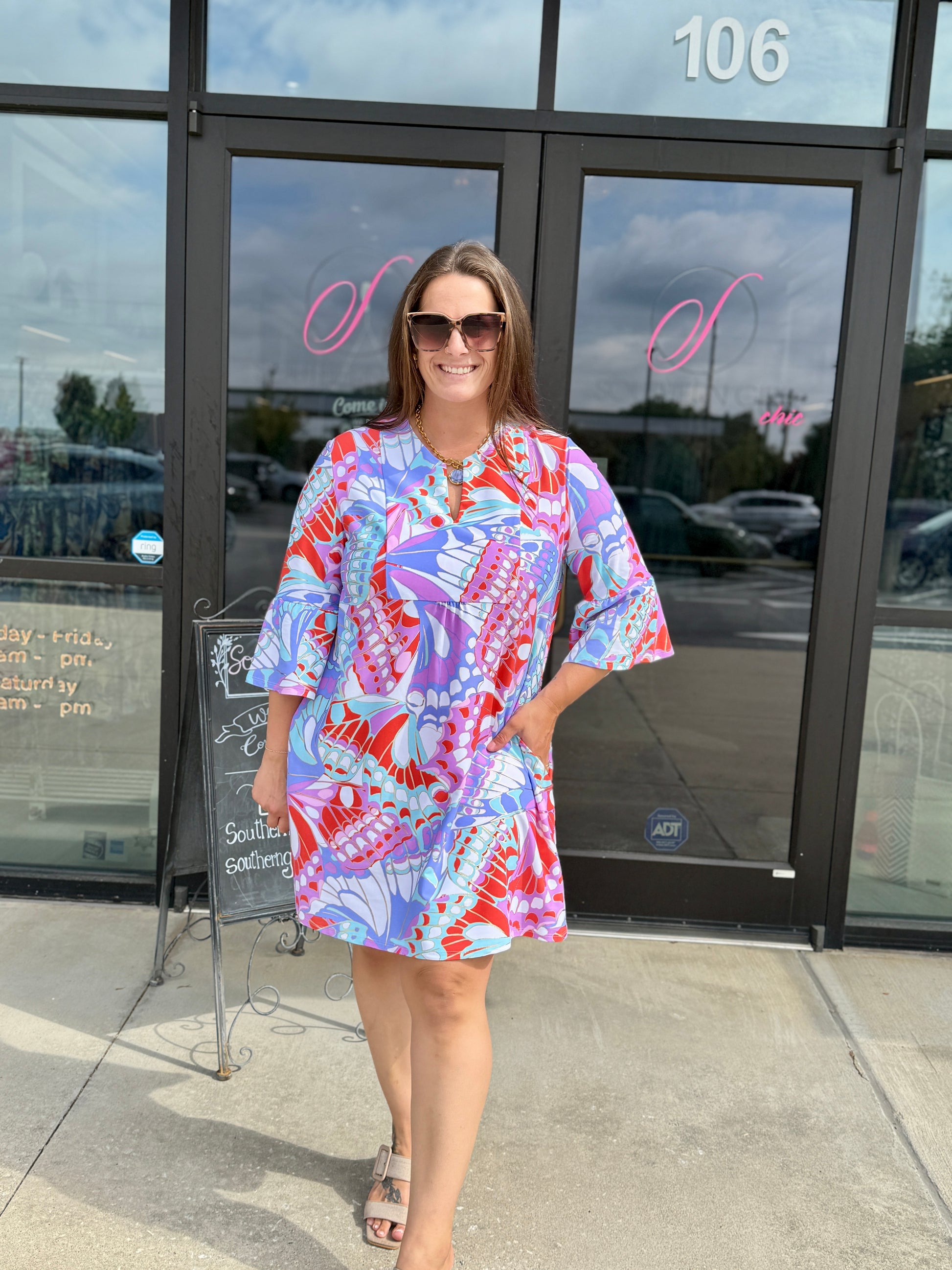 Jude Connally Kerry dress featuring bold butterfly mosaic print, bell sleeves, and V-neckline, worn by smiling woman outdo...