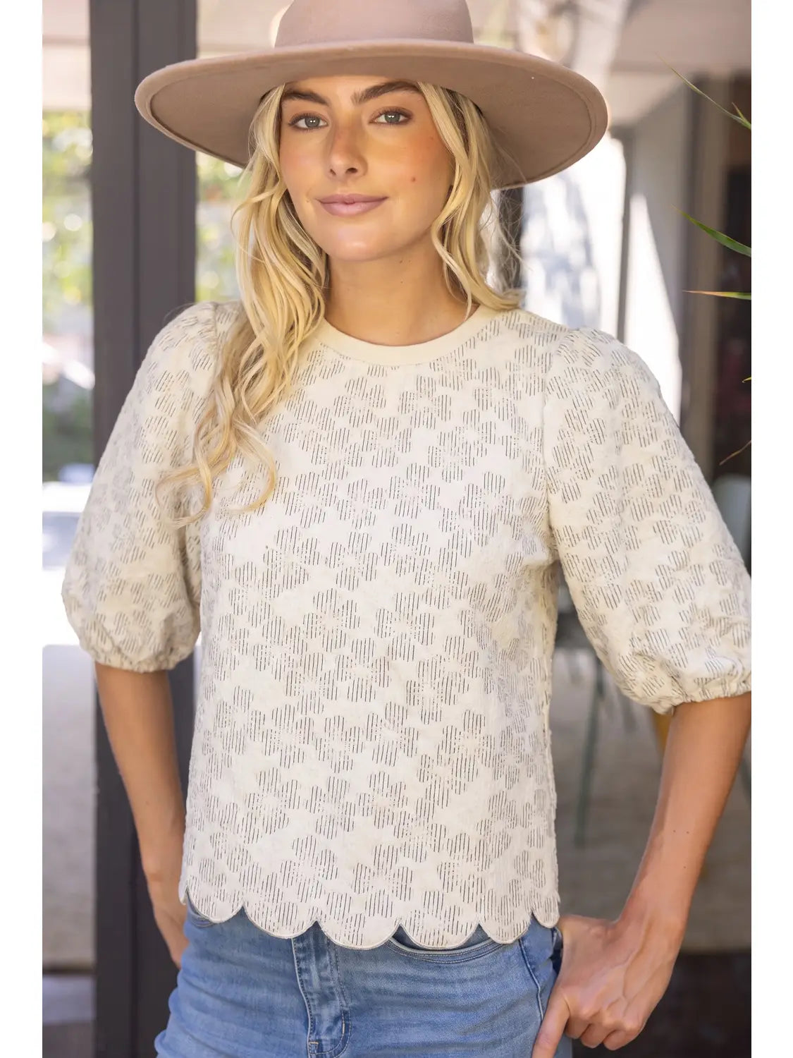 The Willow Bloom scalloped cream textured top with puff sleeves, paired with blue jeans and a wide-brim hat.
