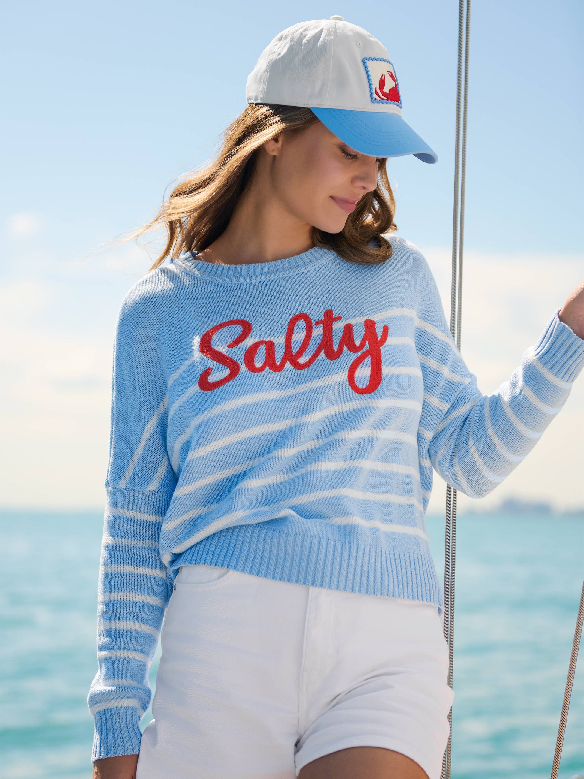 Crab Ball Cap with embroidered patch logo, worn on a sailboat over wavy brown hair.