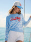 Crab Ball Cap with embroidered patch logo, worn on a sailboat over wavy brown hair.