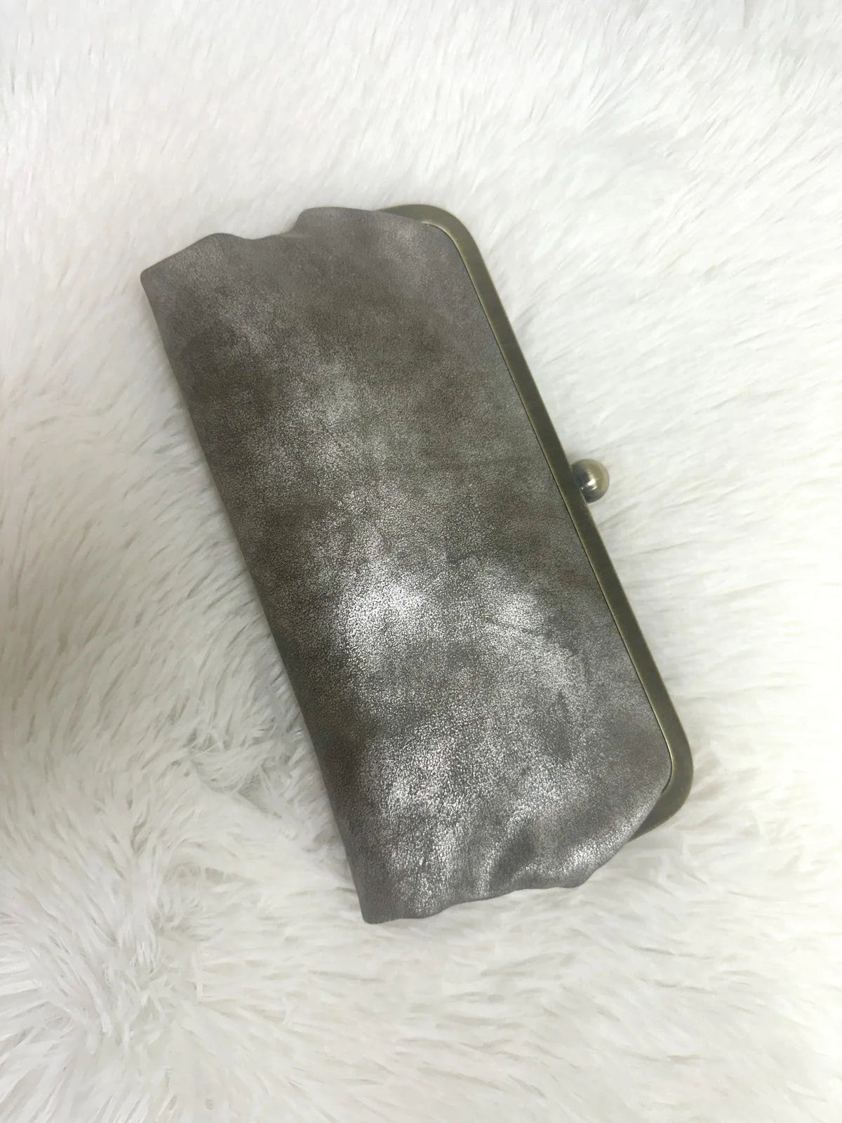 Karen Kiss Lock Clutch in metallic pewter leather with antique silver kiss lock frame closure, displayed on white fur back...