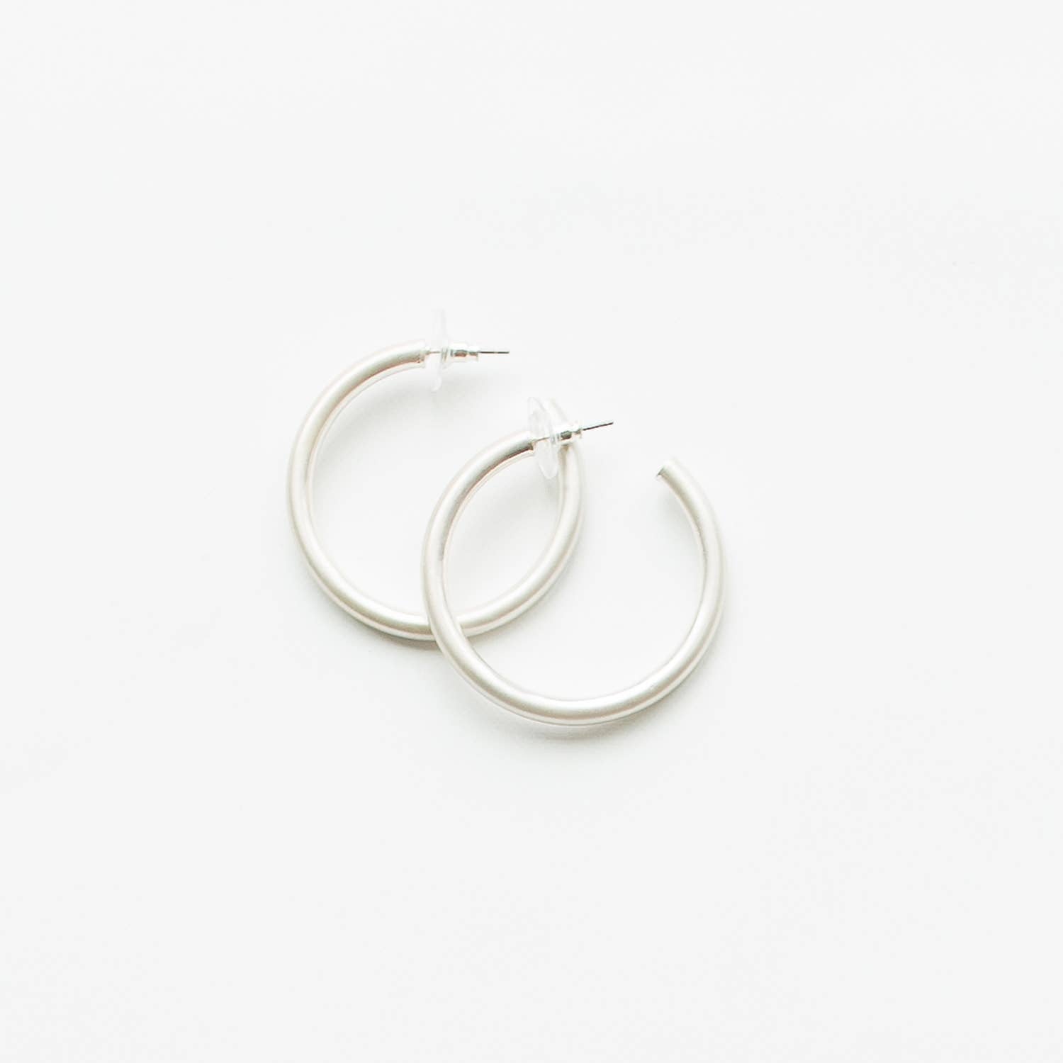 Michelle McDowell Heather Earrings in silver — flat lay of two matte silver tube hoop earrings with post backs.