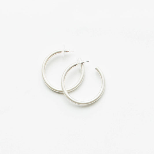 Michelle McDowell Heather Earrings in silver — flat lay of two matte silver tube hoop earrings with post backs.