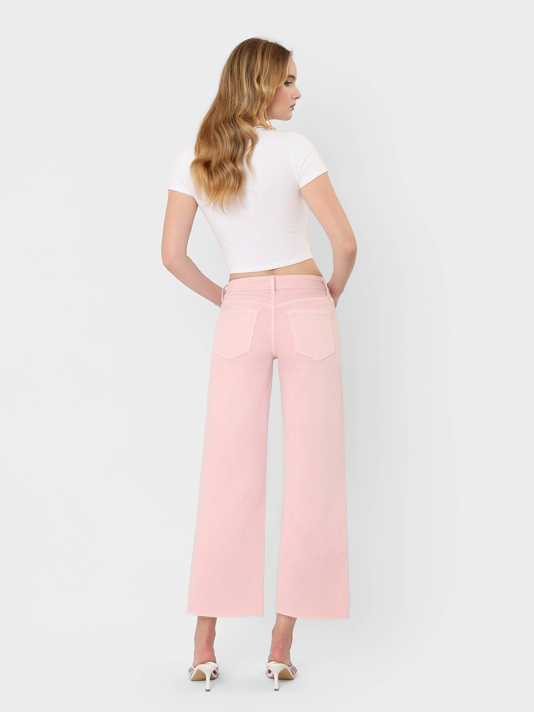 High Rise Crop wide leg jeans in bubblegum pink with raw hem, styled with white crop top and heels.