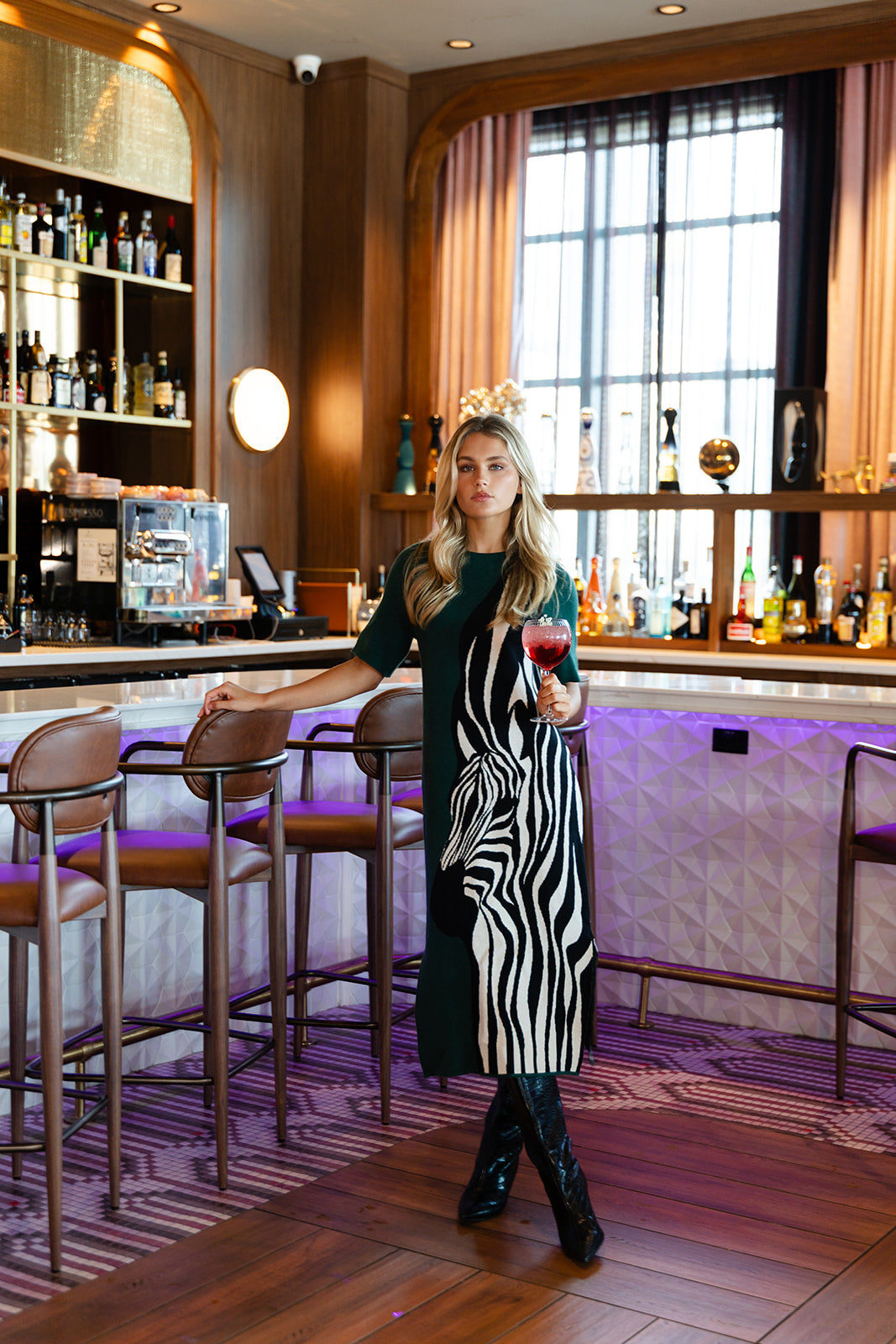 Alden Adair Scout Dress Wild Silhouette — dark green midi dress with bold black-and-white zebra print panel, worn by model at upscale bar