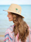 Out Of Office straw fedora sun hat with embroidered palm tree and slogan, worn at beach.