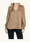 Joy Joy V-Neck Blouse Cafe in warm tan satin, featuring gathered shoulders, blouson sleeves, smocked cuffs, worn by model with black pants.