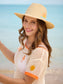 Sunrise Sun Hat wide-brim straw fedora with embroidered sun and wave motifs, worn at the beach.