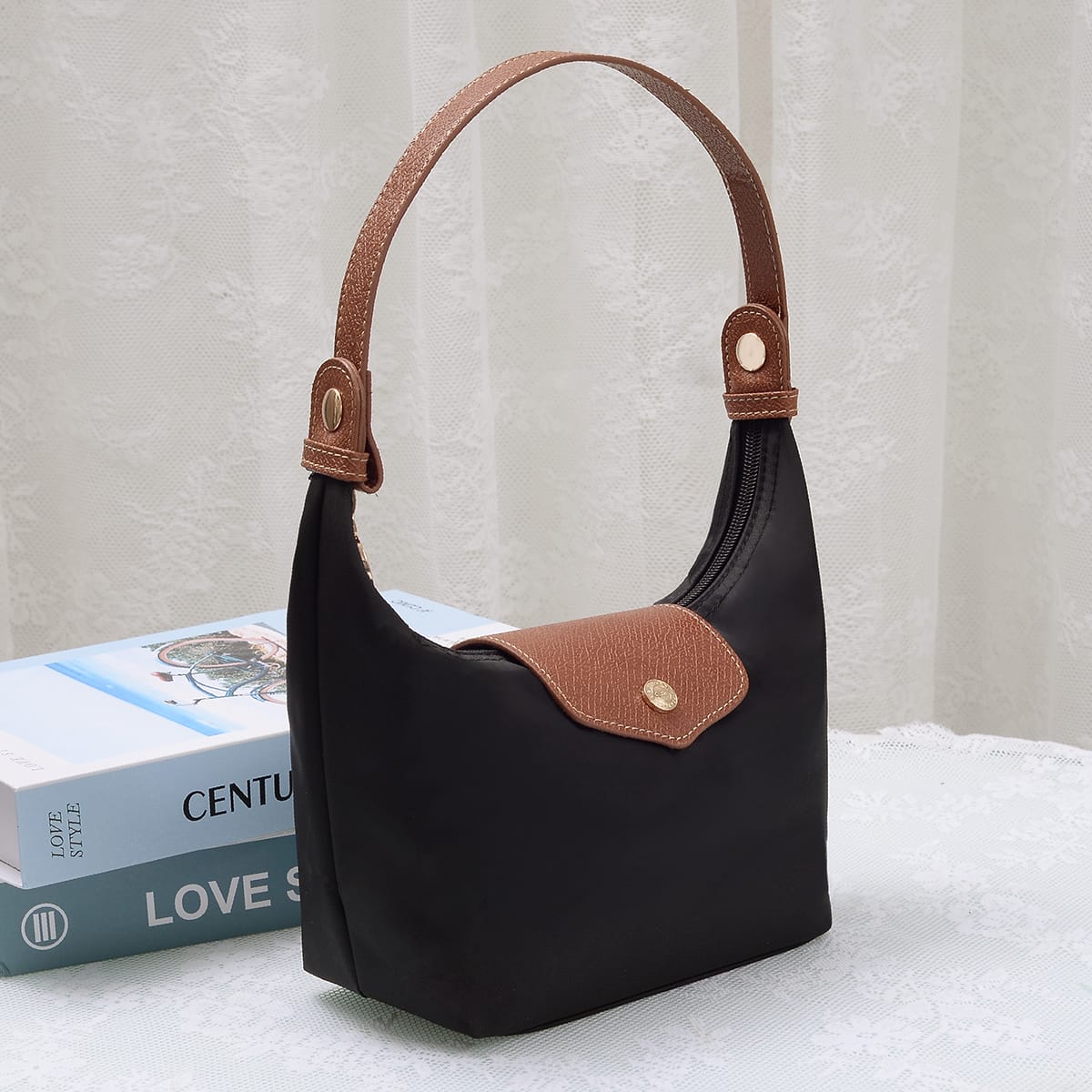 MiMi Wholesale HM780 Nora Nylon Bag in black with tan leather handle and flap detail, styled beside books on a white surface.